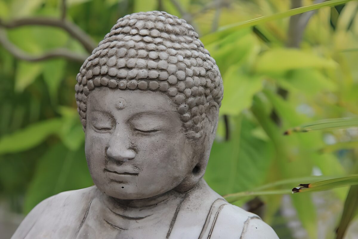 Grå Buddha i ro blandt grønne blade
