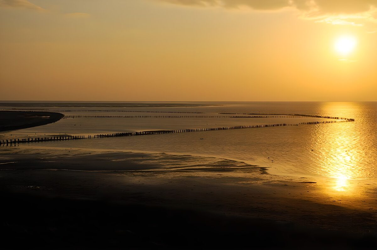 Solnedgang over sand og bølgebrydere