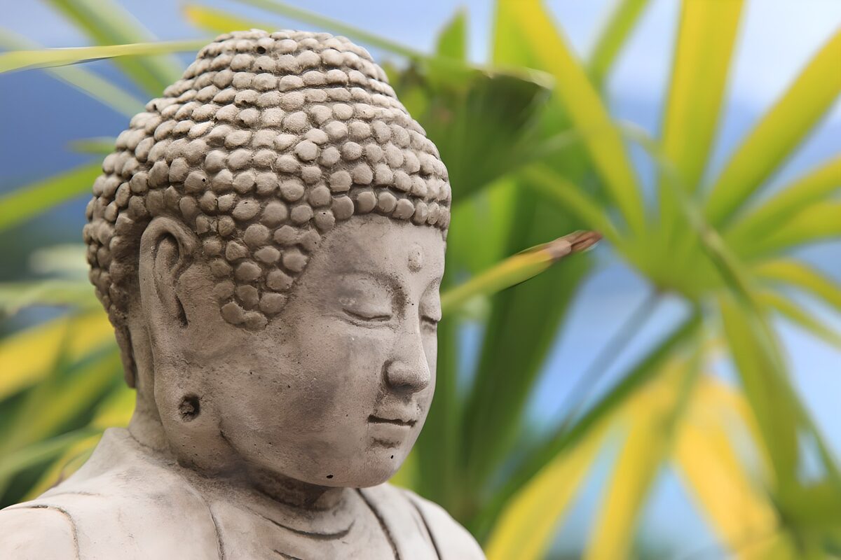 Grå Buddha med grønne blade i baggrunden