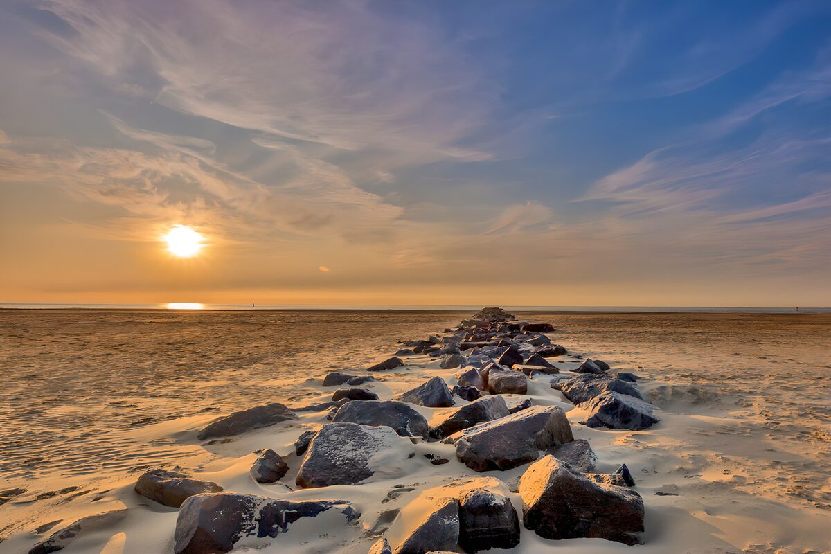 Stenmole på sandstranden i solnedgang