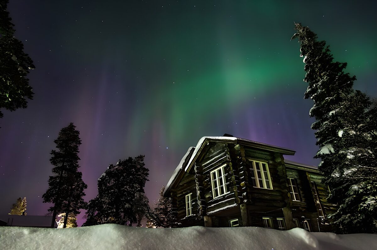 Bjælkehus i sne under nordlys